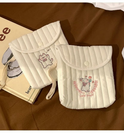 Two white pouches with embroidered designs on a brown surface