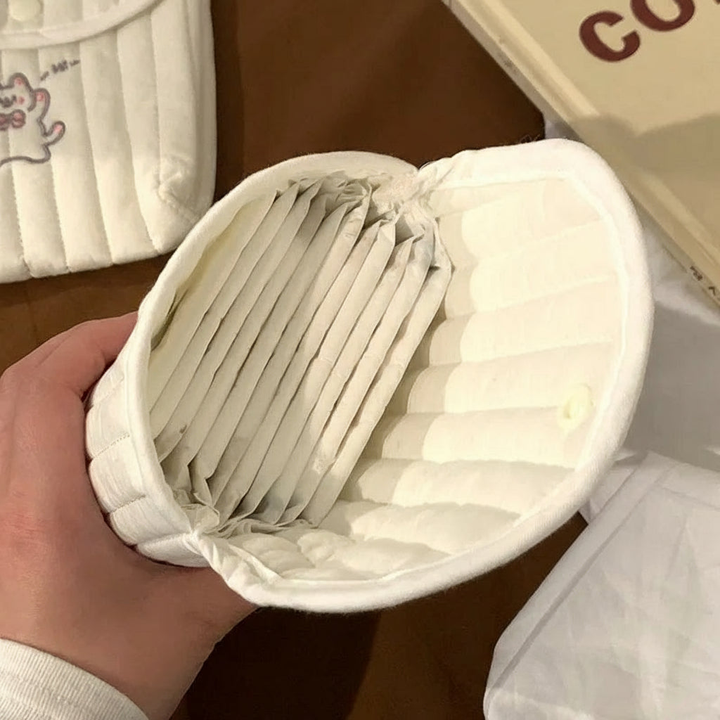 Hand holding a white container with folded items, likely baby wipes, on a wooden surface.